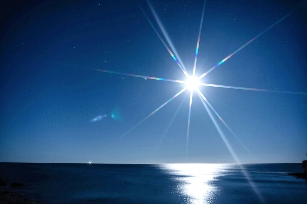 Leuchtender Mond mit Strahlenkranz über dem nächtlichen Meer