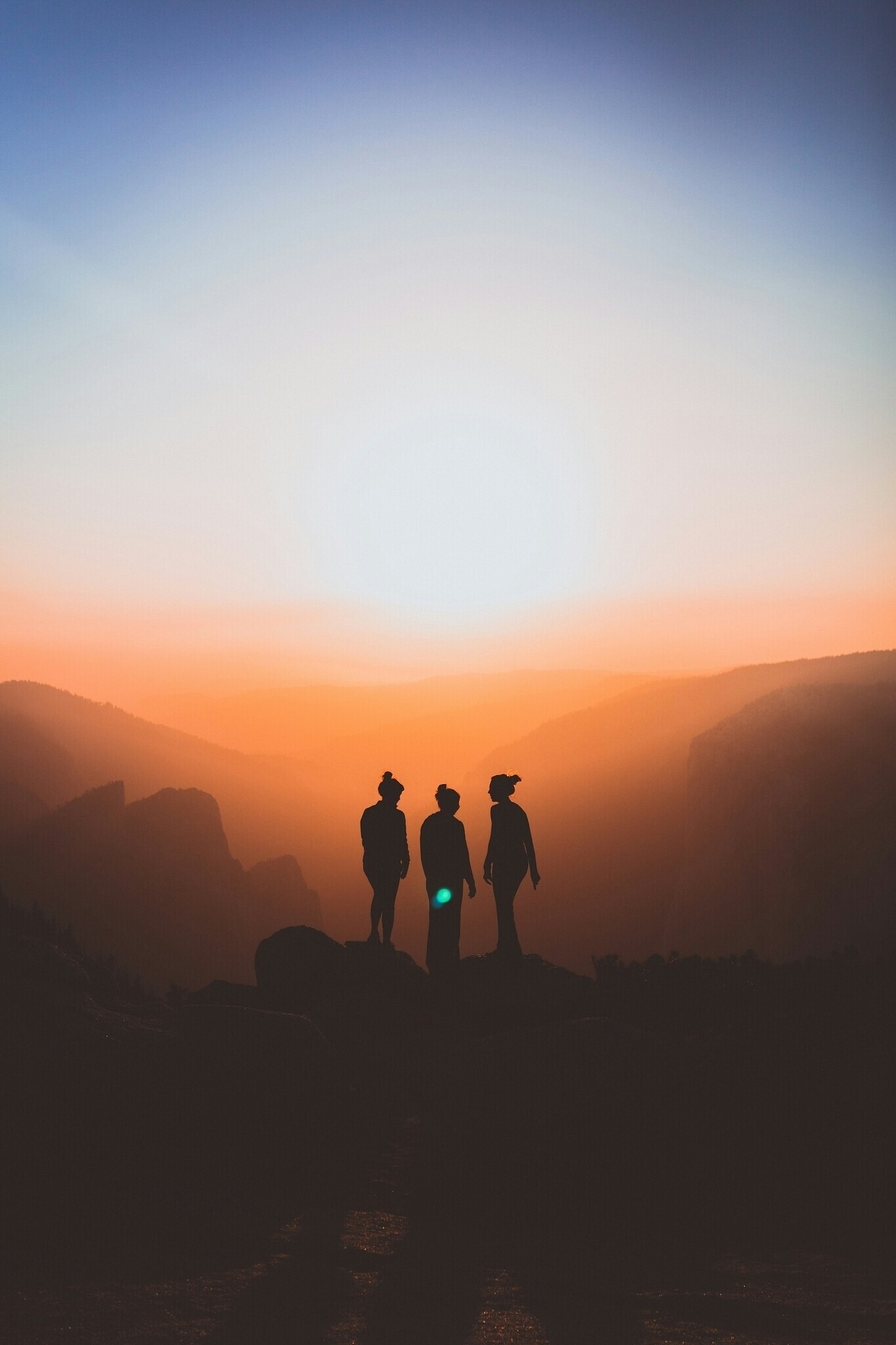 Drei Personen als Silhouetten auf einem Bergrücken bei Sonnenaufgang