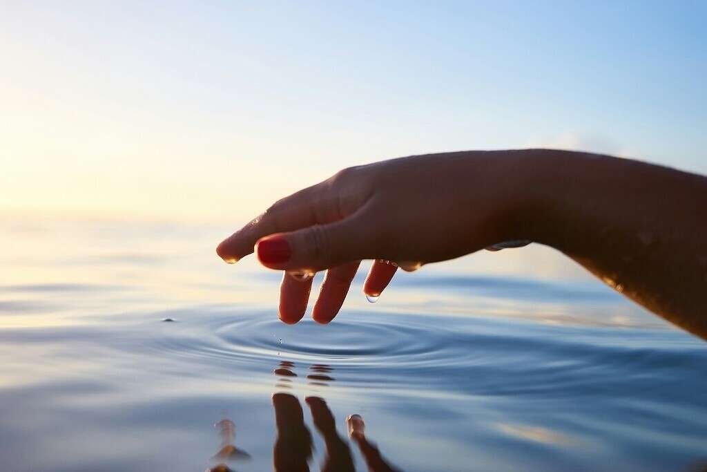 Hand berührt eine ruhige Wasseroberfläche und erzeugt Kreise